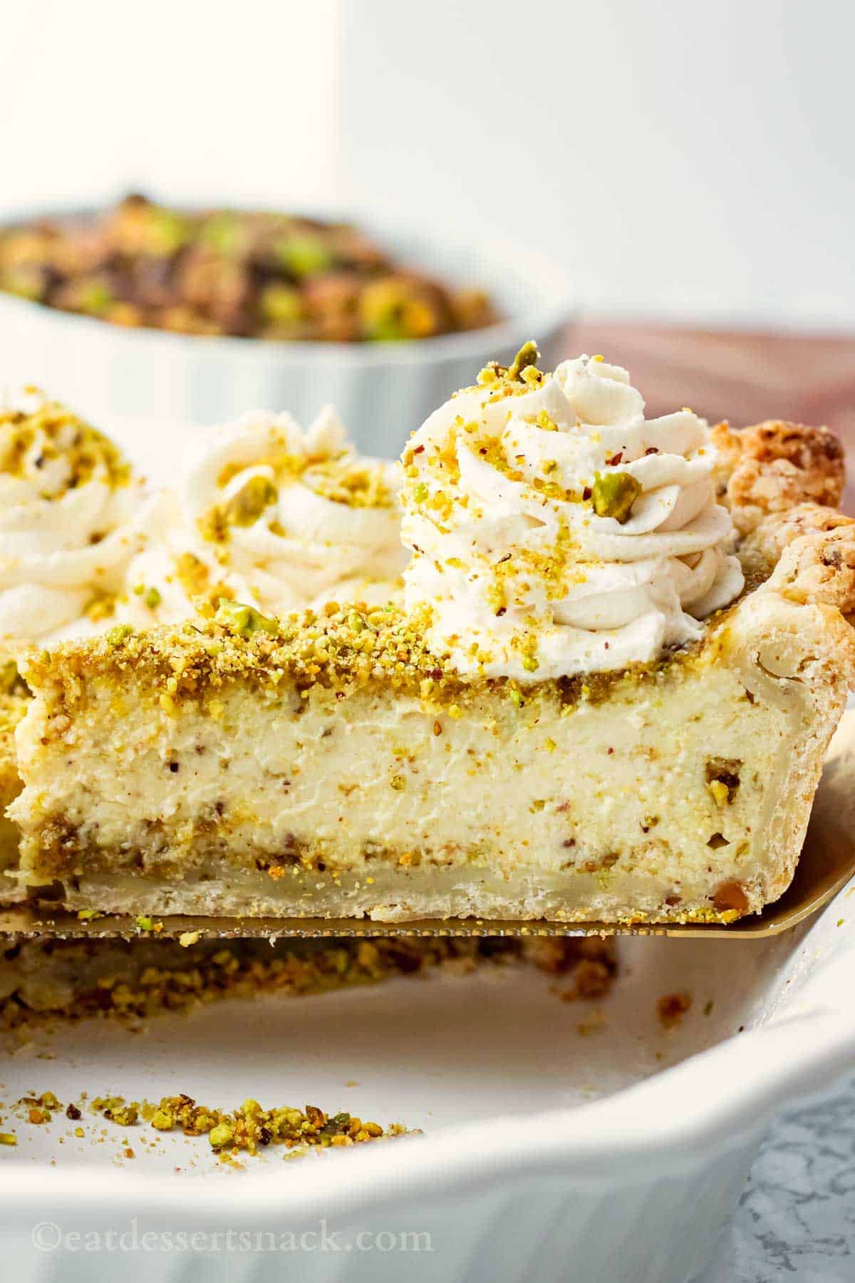 Slice of pistachio custard pie with whipped cream on spatula.