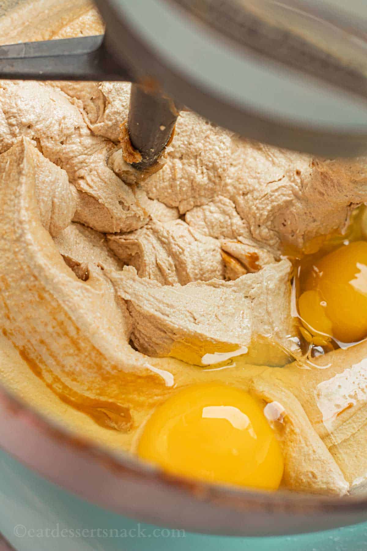 Raw eggs in sugar and butter mixture for cookies in metal mixing bowl.