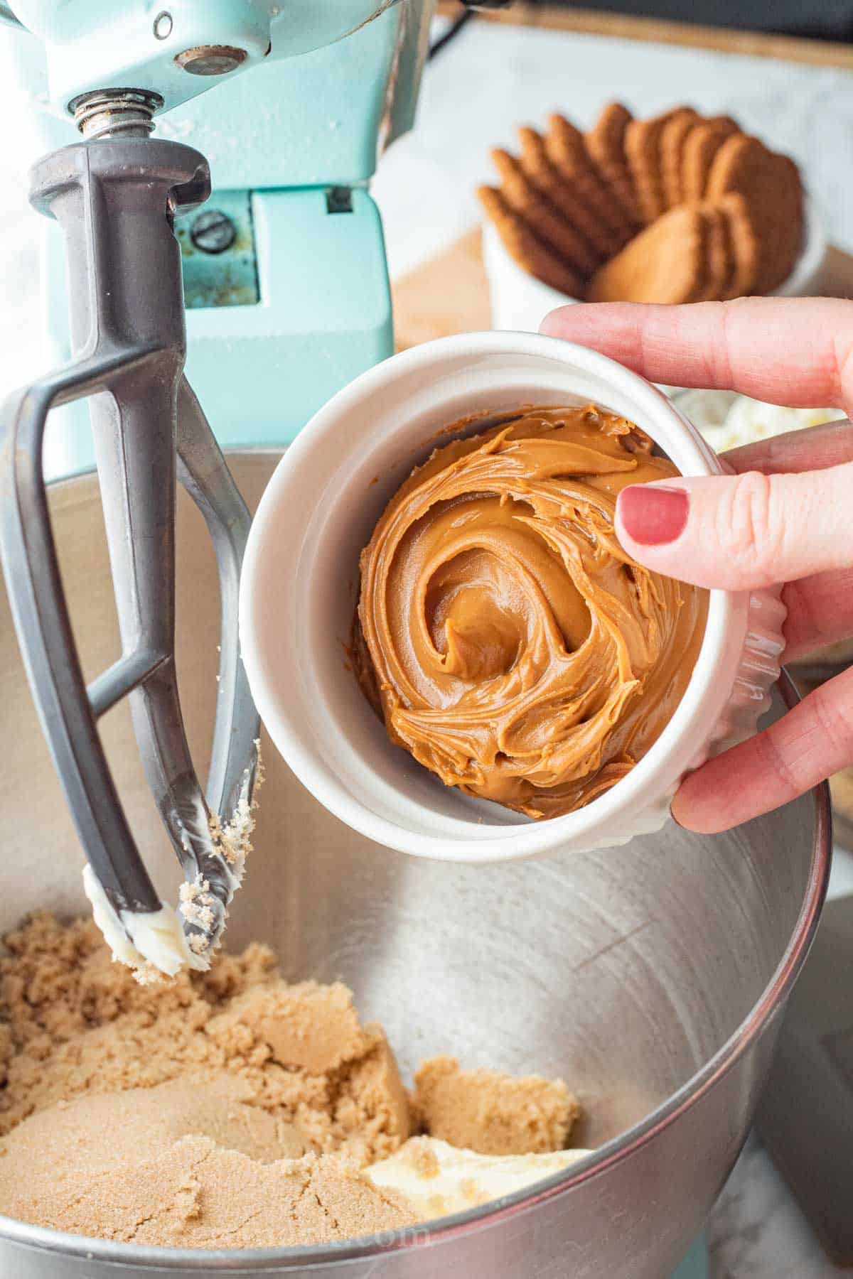 White bowl of cookie butter pouring into metal mixing bowl.