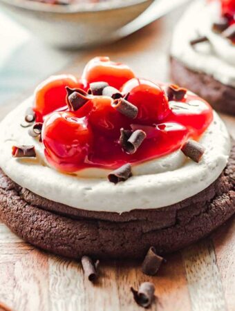 Baked cherry chocolate cheesecake cookie with chocolate shavings on wood board.