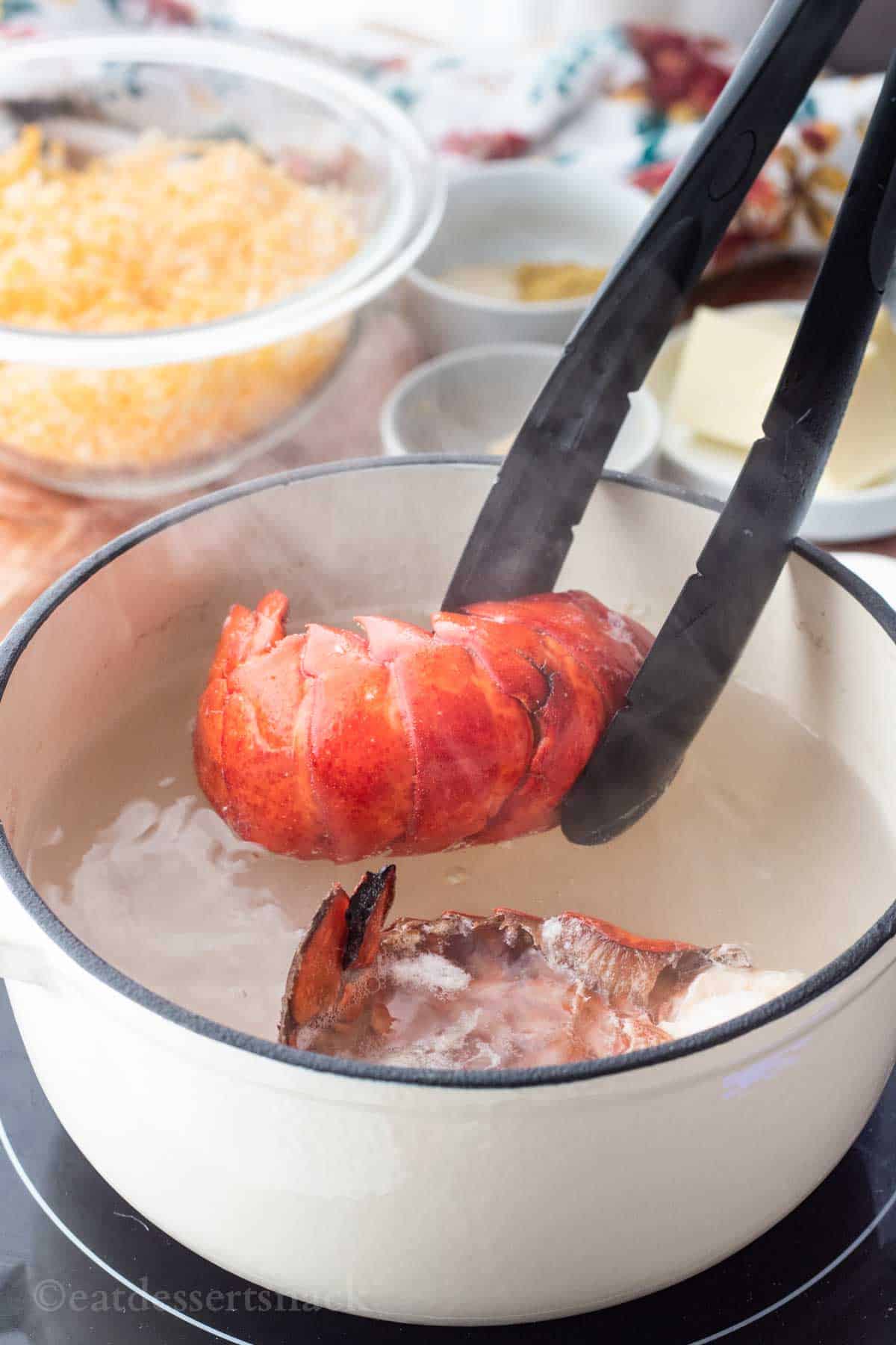 Black tongs removing red lobster tail from white enamel pot of hot steamy water.