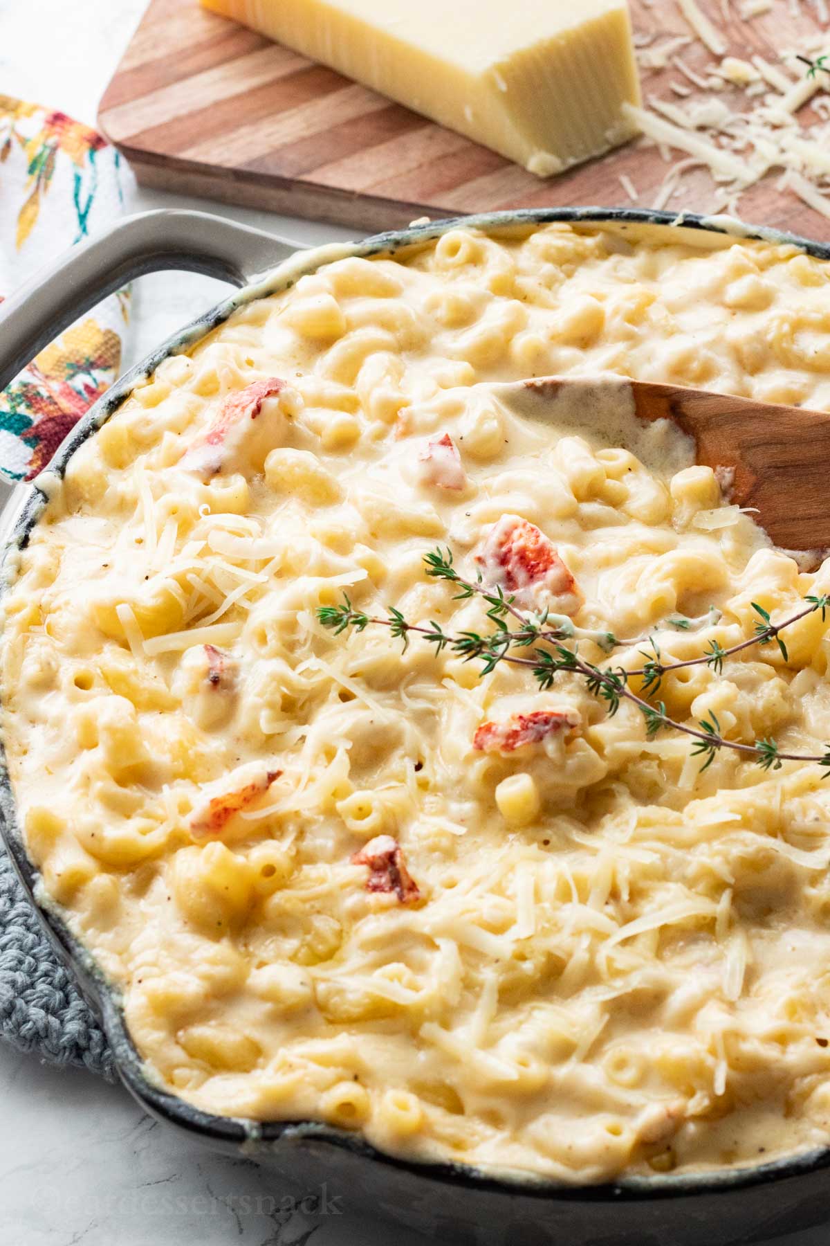 Gray frying pan very full of melted cheesy lobster mac and cheese with fresh thyme on top.
