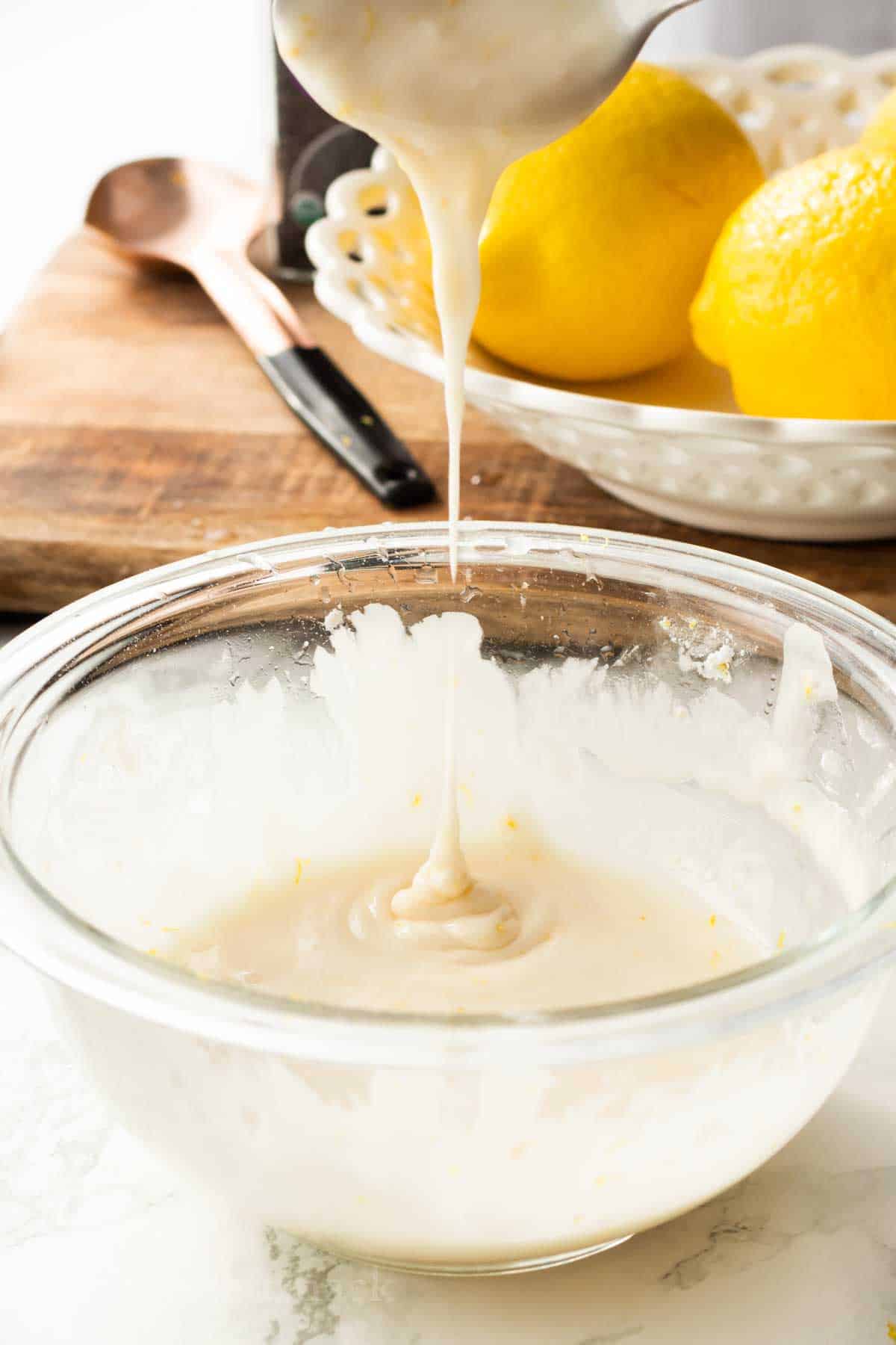 Spoon drizzling lemon icing into glass bowl.