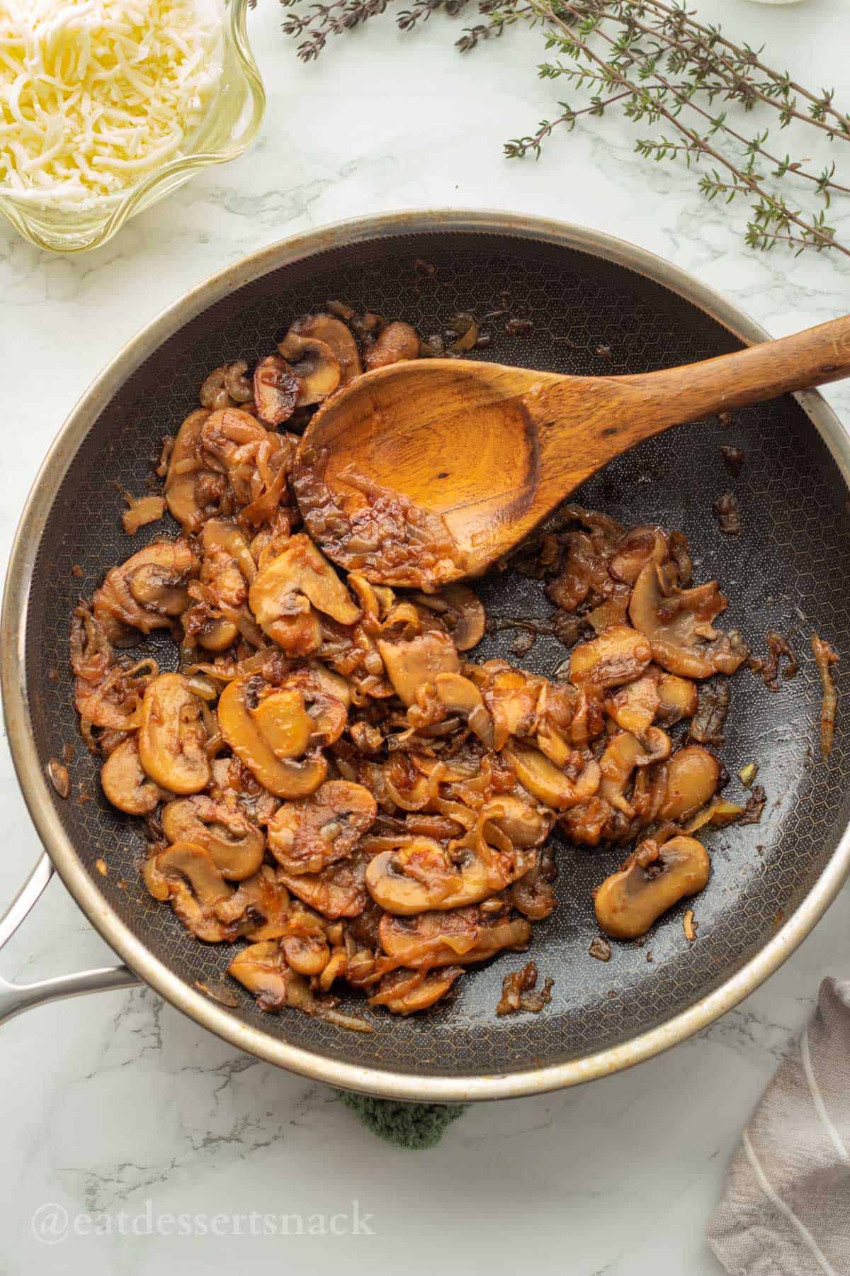 Cooked mushrooms and onions with wooden spoon in metal pan.