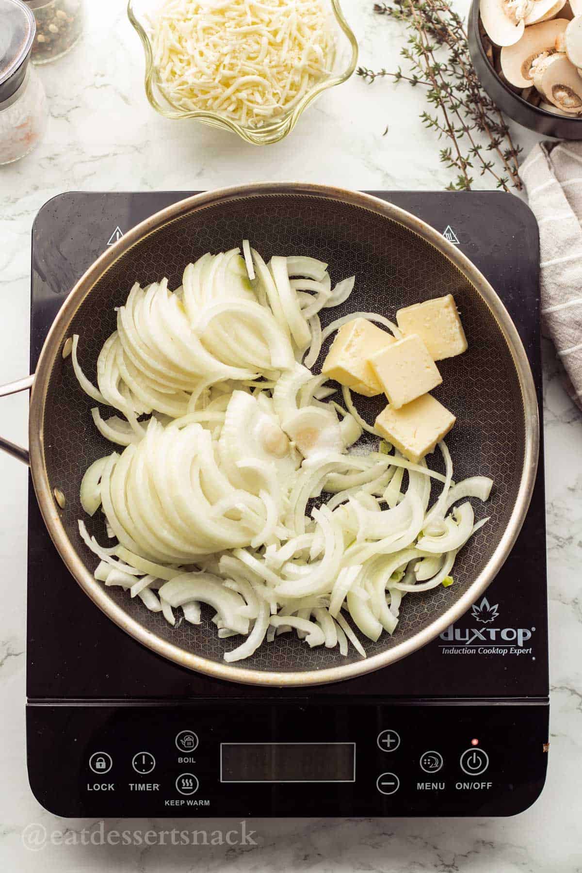 Raw onions with butter in metal pan on cooktop.