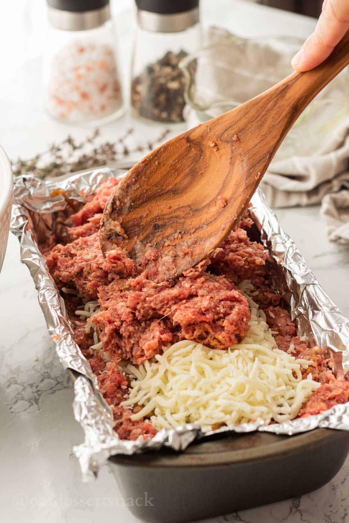 Wooden Spoon spreading raw meat onto cheese and mushroom filling.