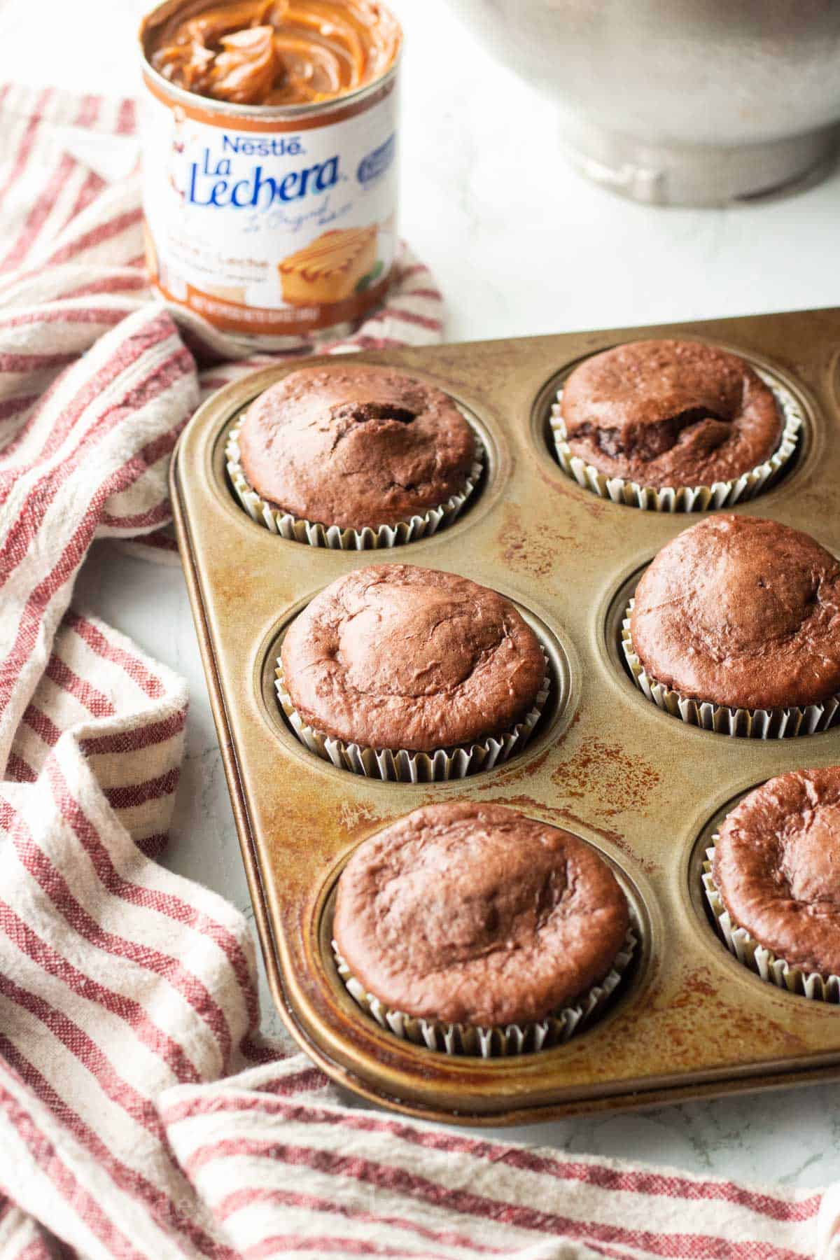 Baked chocolate cupcakes in metal pan with can of dulce de leche behind.