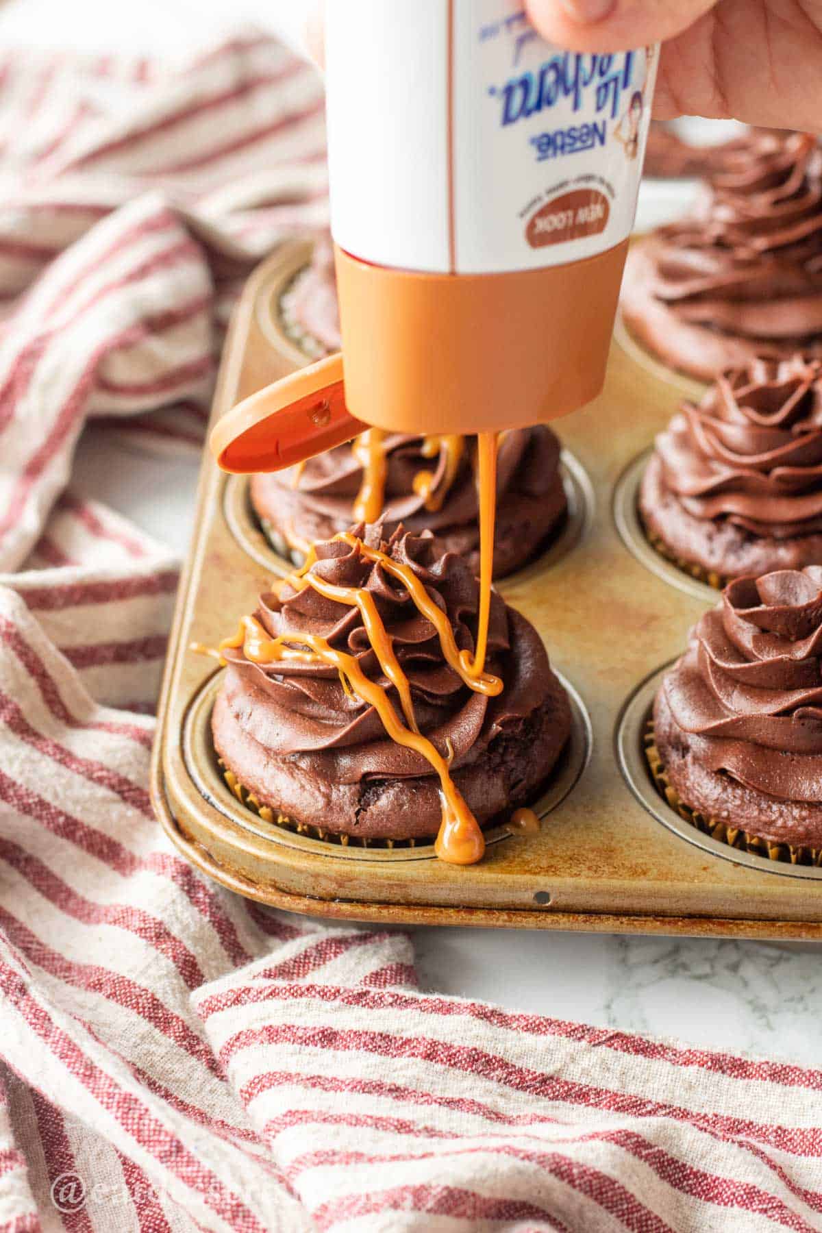 Pouring caramel drizzle over chocolate frosted cupcakes.
