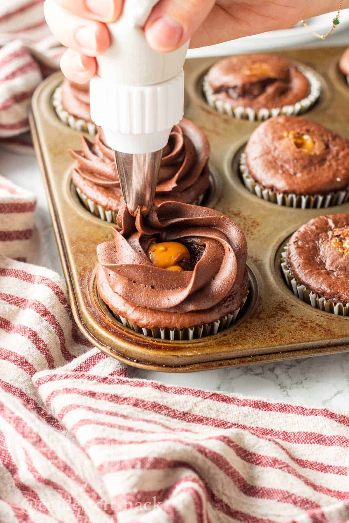 Hand piping chocolate frosting onto caramel filled chocolate cupcakes.