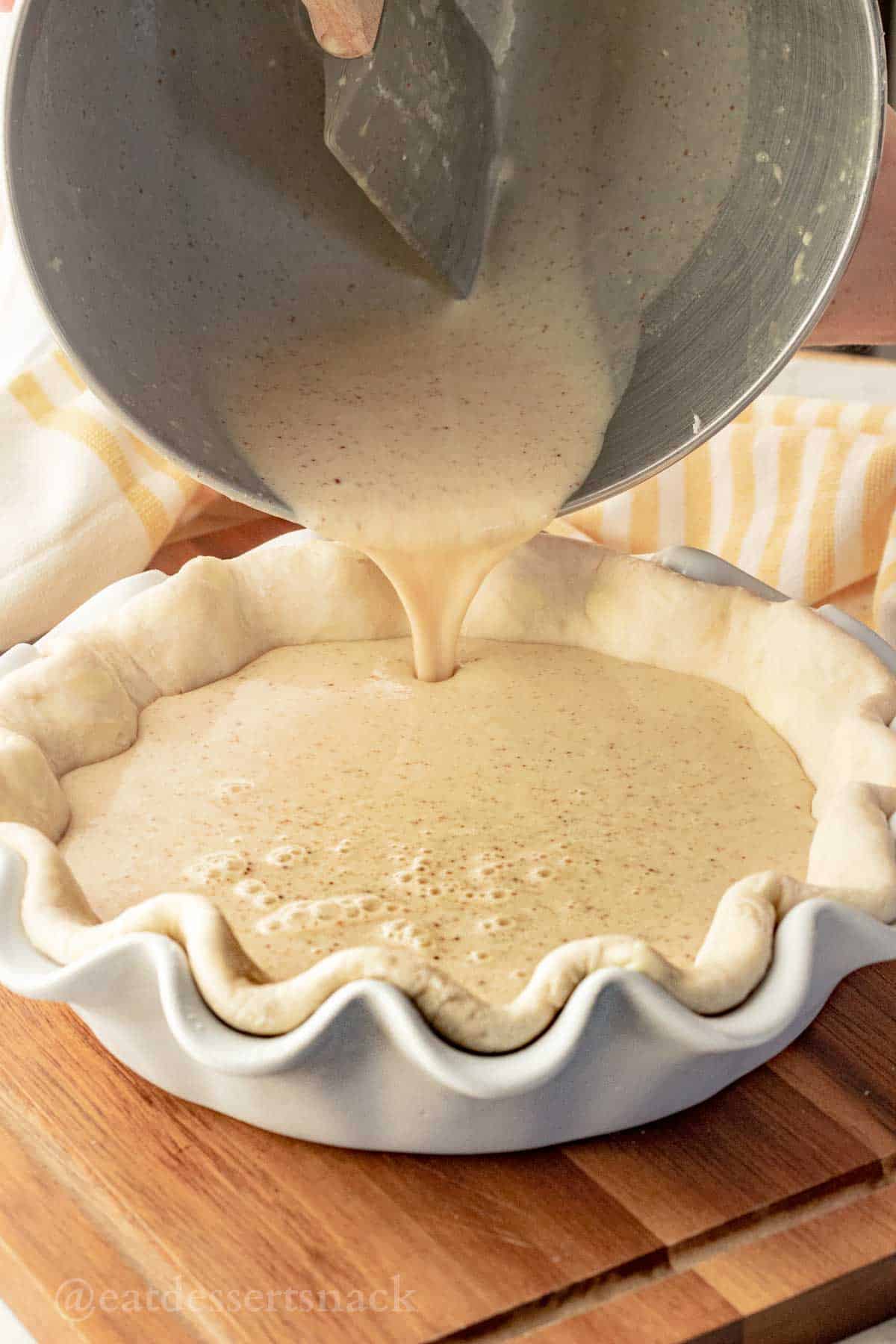 Pouring raw banana custard filling into raw pie shell in white ceramic pie pan.