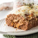 Cooked meatloaf stuffed with mushrooms and cheese on white platter with thyme on top.