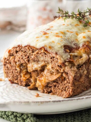Cooked meatloaf stuffed with mushrooms and cheese on white platter with thyme on top.