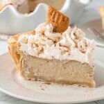 Single slice of baked banana pie with whipped cream and cinnamon on top, sitting on a white plate.