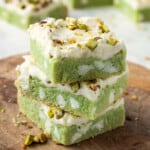 Stack of baked frosted pistachio ars on wood board.