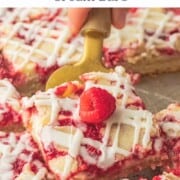 Gold spatula with slice of raspberry cream bar and fresh raspberry on top.