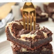Stack of 3 slices of baked cheesecake brownie bars with gold fork in them.