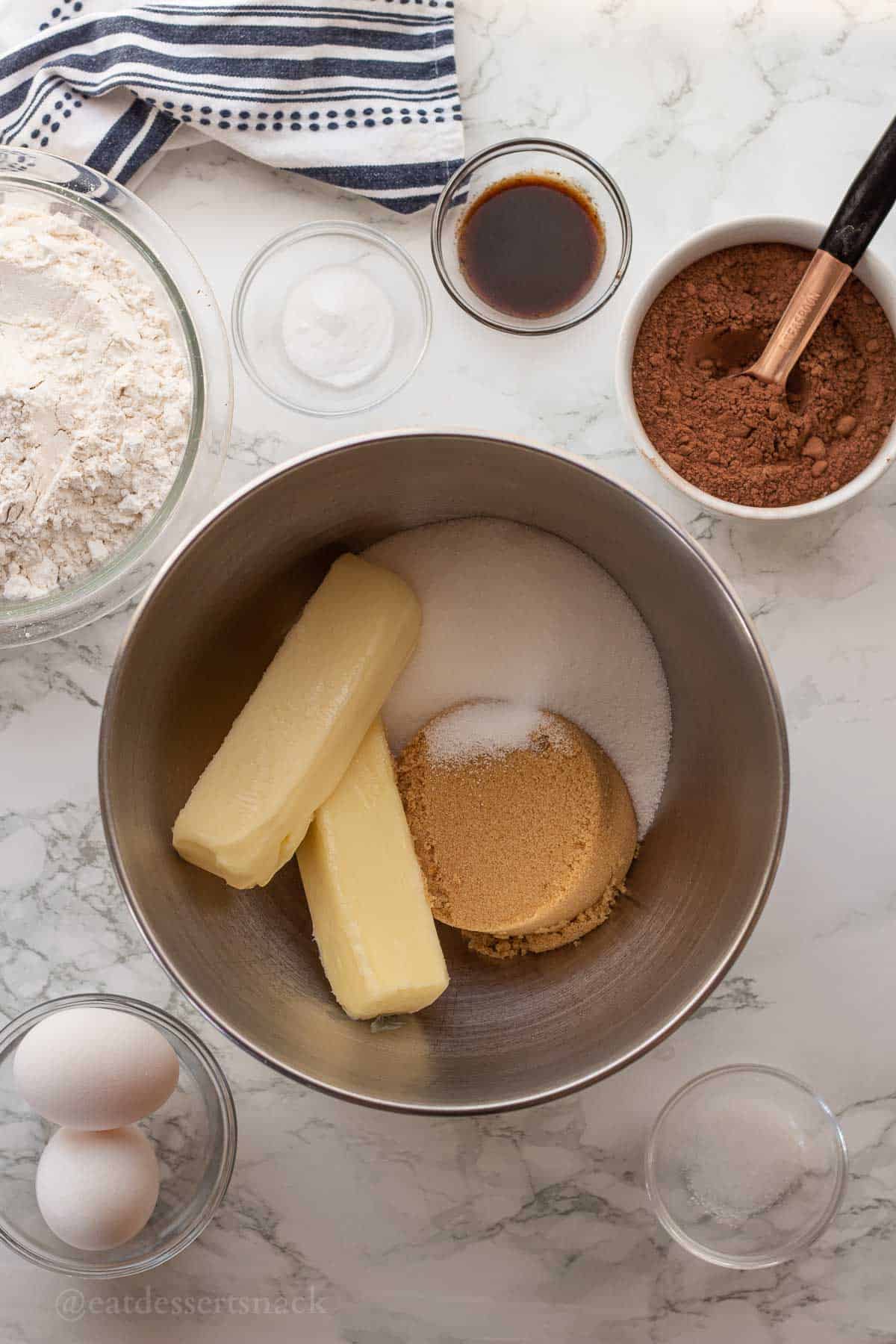 Butter, brown sugar, and white sugar in metal bowl with other ingredients nearby in glass bowls.