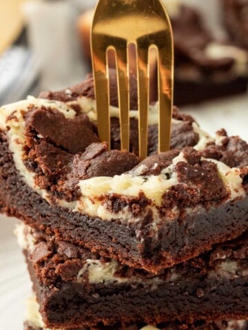 Stack of 3 baked cheesecake brownie bars with gold fork.