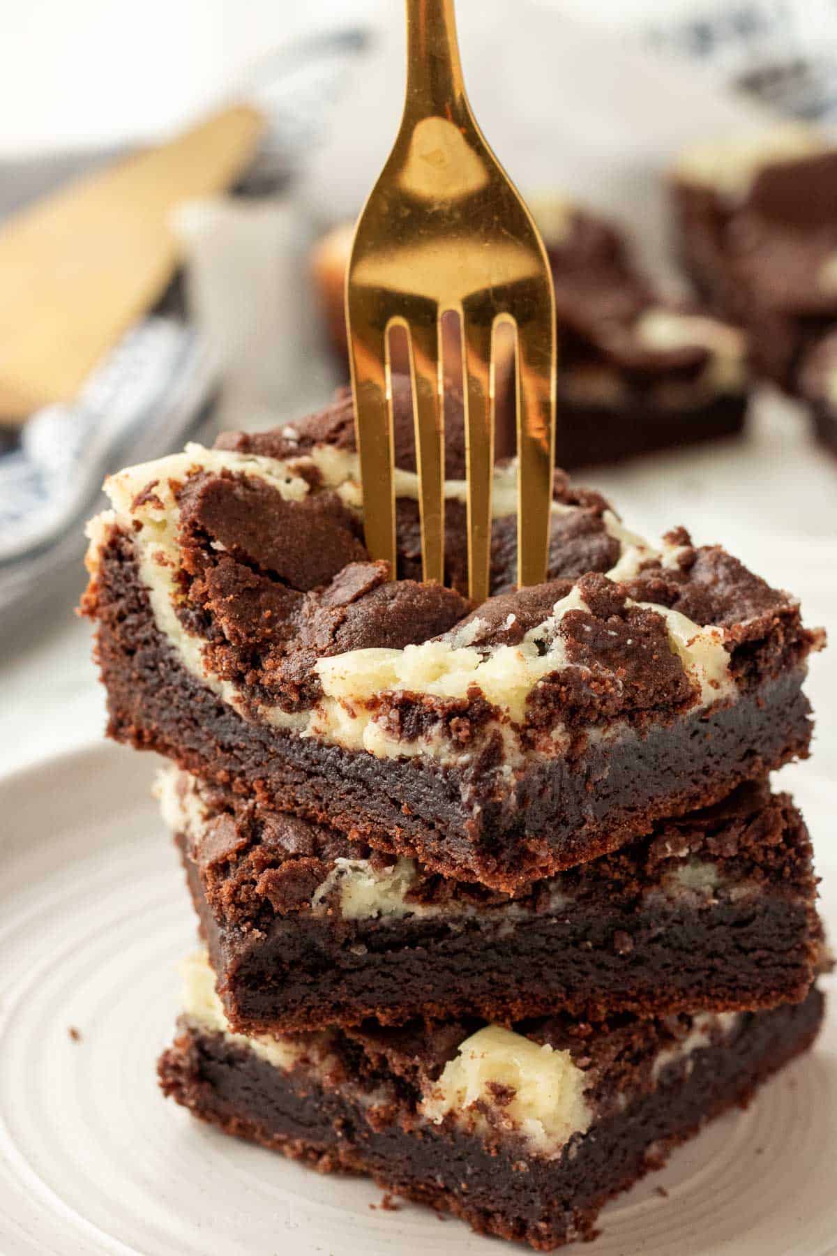 Stack of 3 baked cheesecake brownie bars with gold fork.