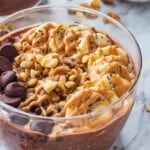Chocolate peanut butter overnight oats in glass bowl with bananas, chocolate chips, and walnuts on top.