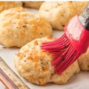 Red brush with butter on baked cheddar drop biscuit.