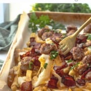 Fork with bite of french fries, cheese, sausage, and bacon on top.