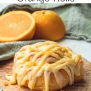 Baked and frosted orange roll on wood cutting board.
