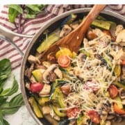 Cooked chicken, zucchini, tomatoes, and mushrooms in metla pan with wooden spoon.