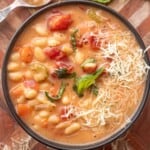 Bowl of cooked tuscan white bean soup on wooden cutting board with basil and shredded parmesan.