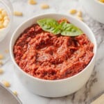 White bowl of pesto rosso red pesto sauce on marble countertop.