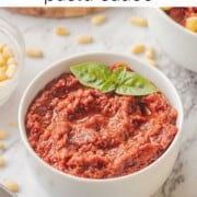 Blended red pesto with basil leaf in white bowl on marble countertop.