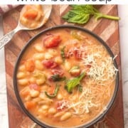 Bowl of cooked tuscan white bean soup on wooden cutting board with basil and shredded parmesan.