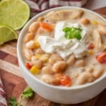 White bowl with cooked white chicken chili with cilantro and sour cream.