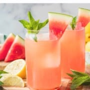 Glass of watermelon mint lemonade on wood cutting board with slice of watermelon and sprig of mint on top.