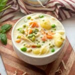 White bowl of chicken gnocchi soup on wood cutting board.