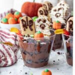 Clear clup of pudding and oreos with worms, pumpkin candy, sprinkles, headstone cookie, and mummy cookie.