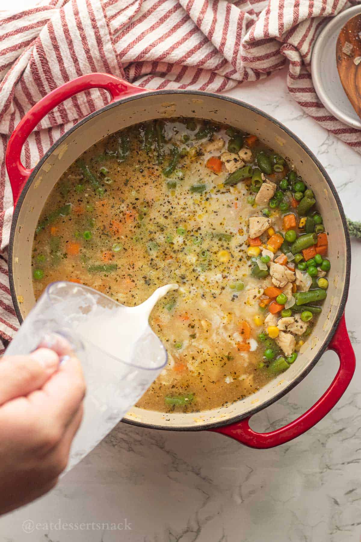 Milk pouring into red pot of chicken soup.