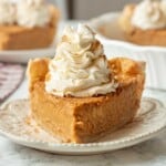 Slice of cream cheese pumpkin pie with whipped cream on white plate.