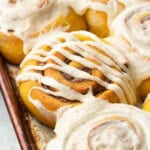 Baked frosted pumpkin cinnamon rolls in metal pan.