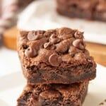 Stack of baked chocolate chocolate chip cookie bars on white plate.