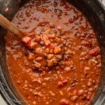 Cooked ladleful of turkey chili in black crockpot.