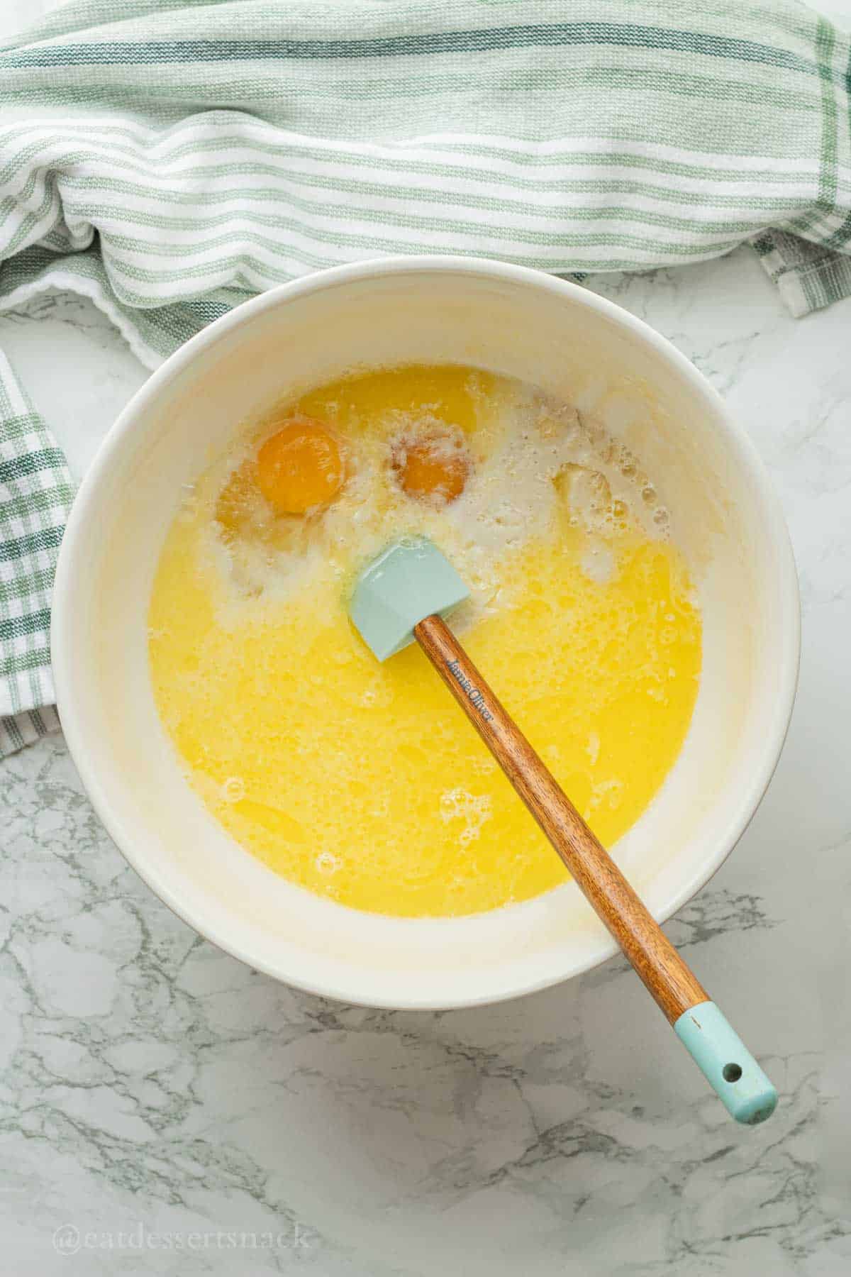 Eggs, melted butter, milk, and sourdough discard in white bowl with rubber spatula.