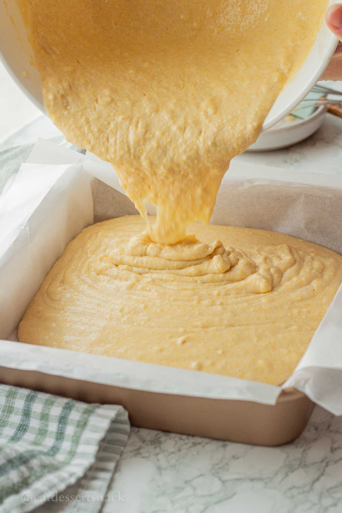 Pouring raw cornbread batter into metal baking dish.