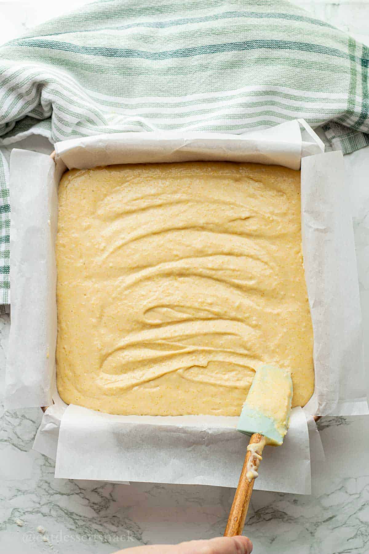 Smoothing out raw cornbread batter in baking dish.