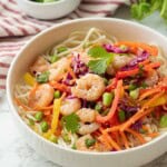 Chopped veggies in white bowl with cooked shrimp over bed of noodles.