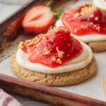 Baked strawberry cheesecake cookie on baking sheet with fresh strawberry.
