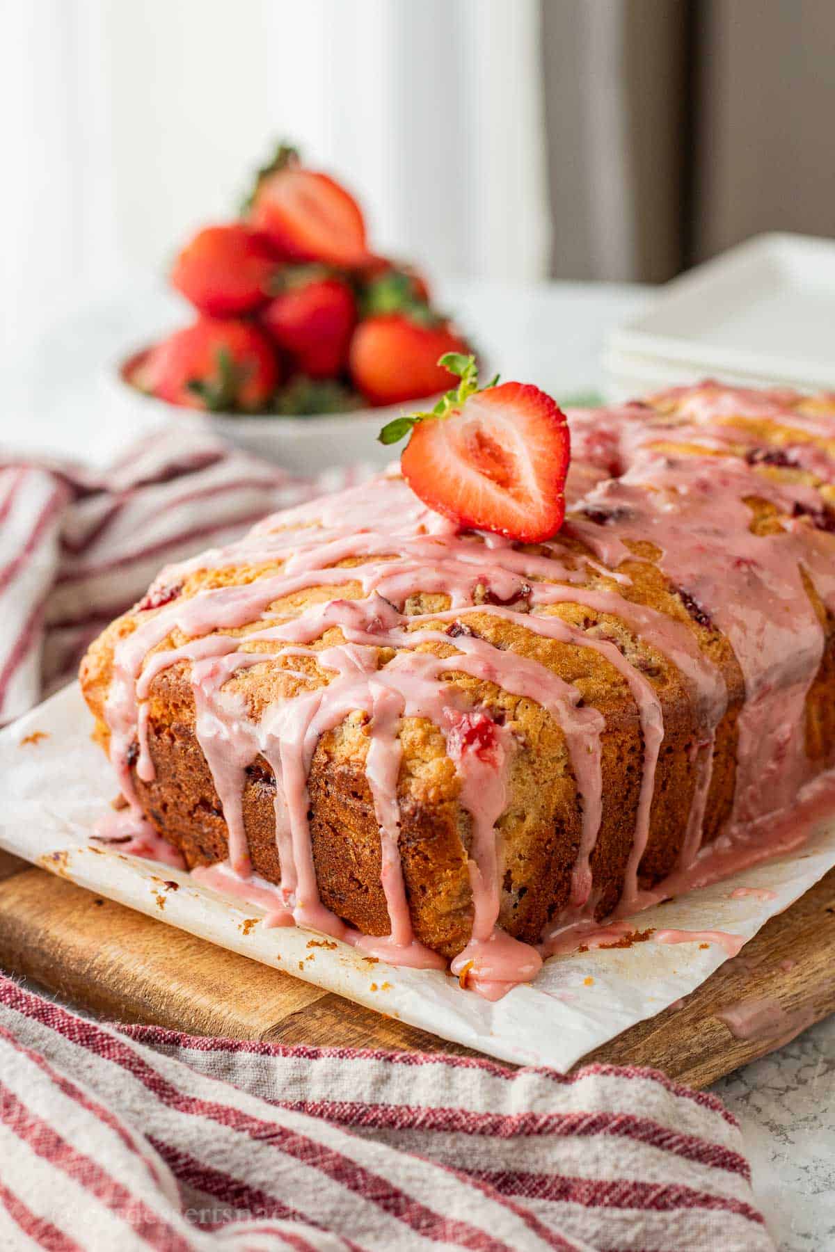 Baked loaf of strawberry banana bread with icing and strawberry on top.