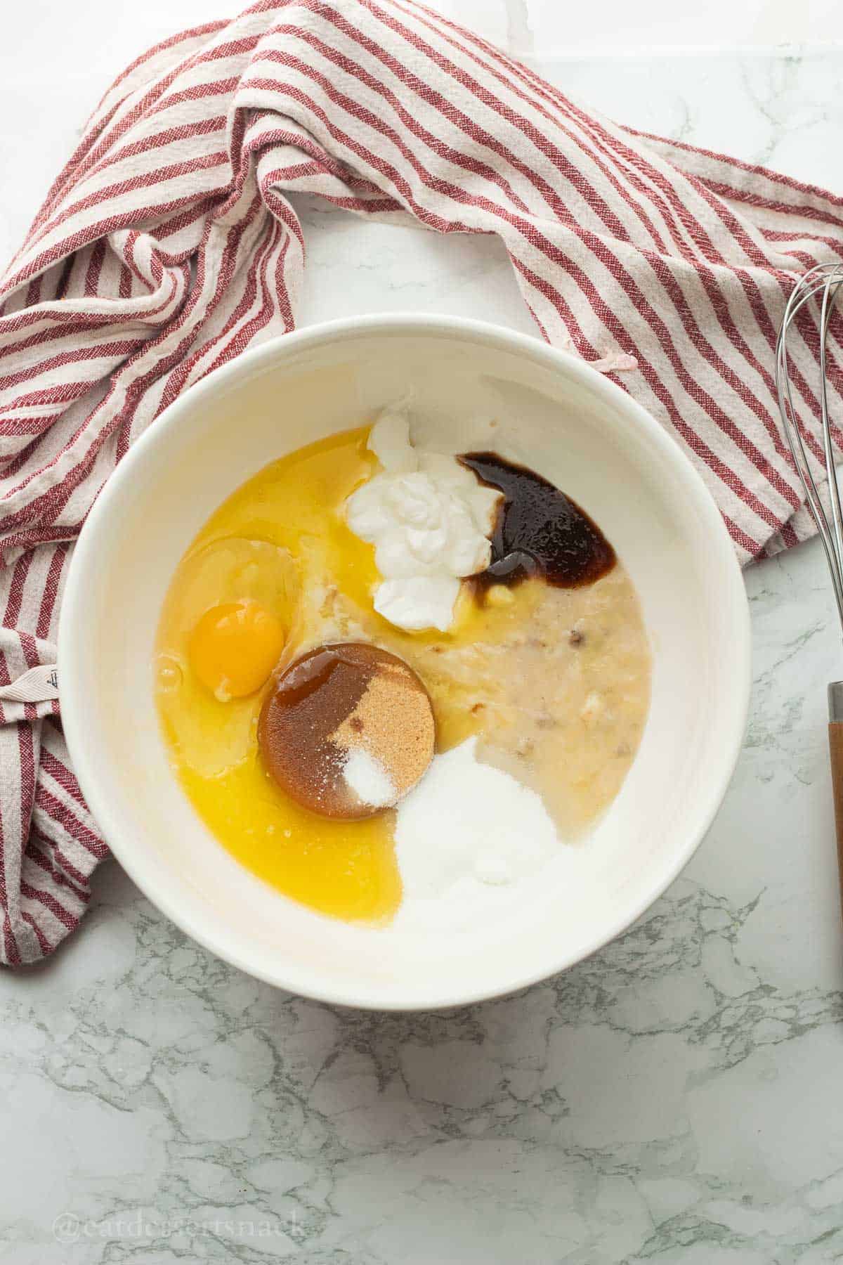 Brown sugar, egg, sour cream, vanilla, and bannaa in white bowl.