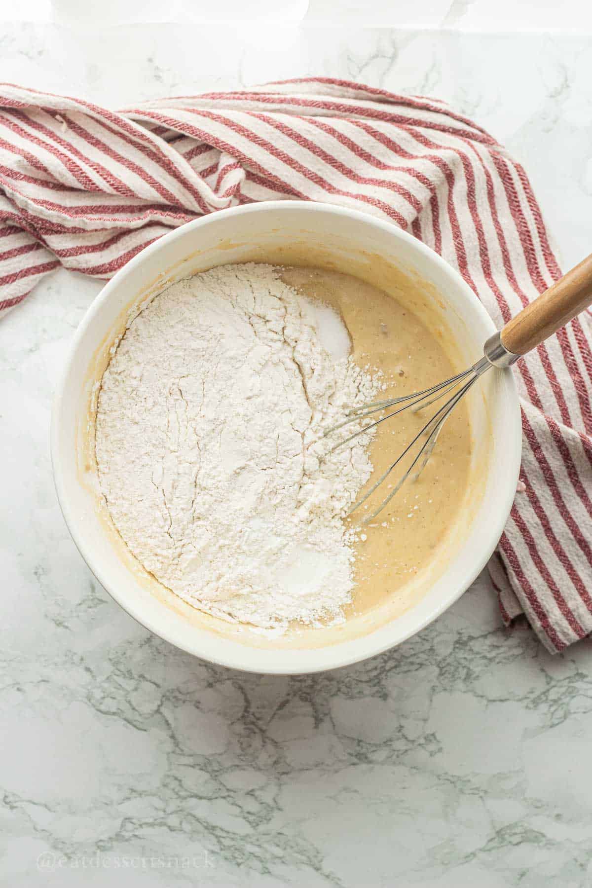 Flour, baking powder, and salt in white bowl with wet ingredients.