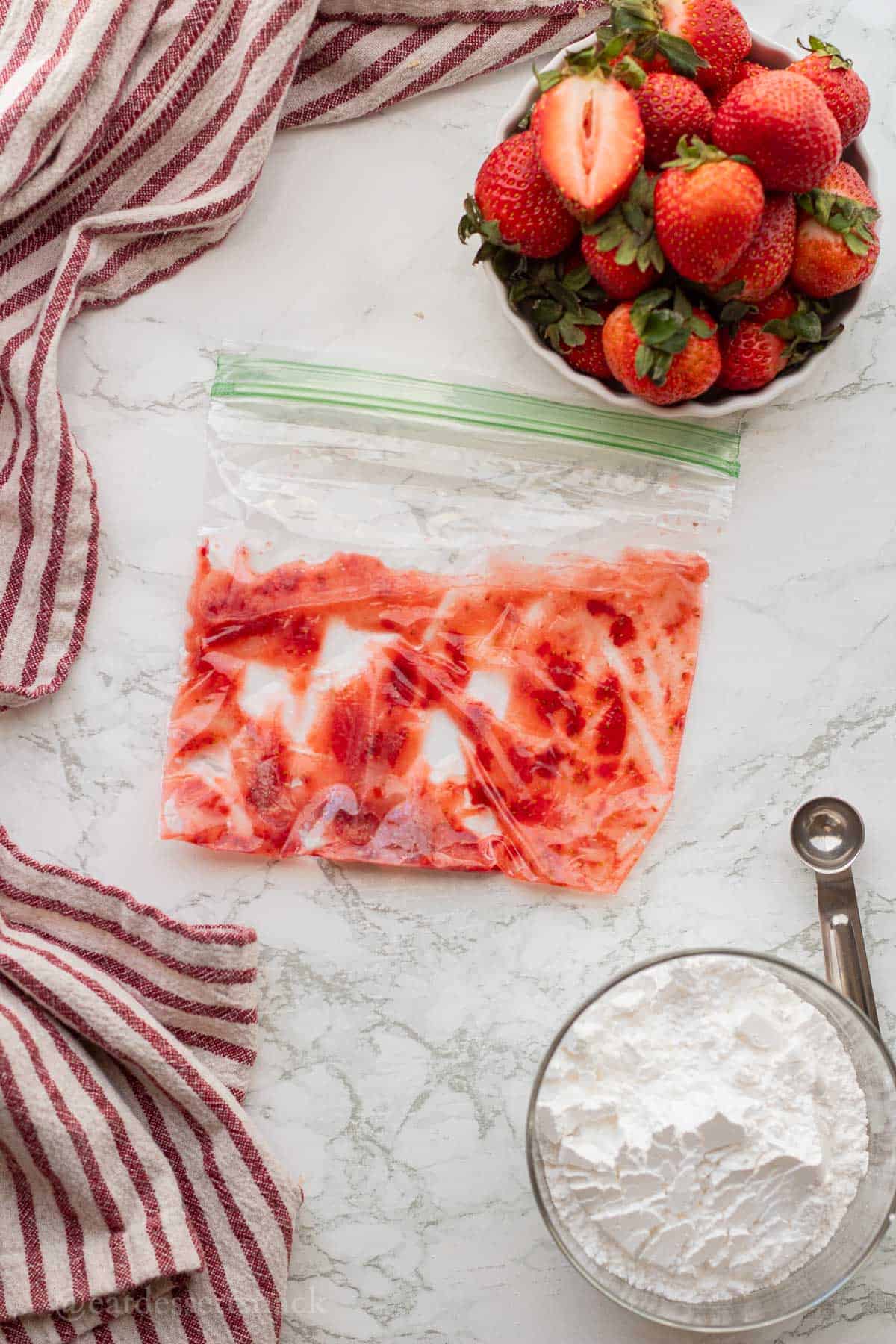 Mashed strawberries in bag on marble countertop.